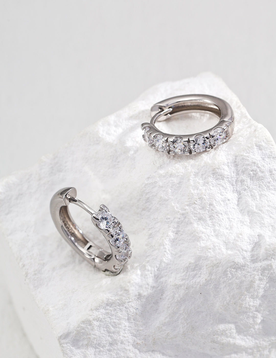 A pair of cubic zirconia diamond hoop earrings resting on a rugged rock, showcasing their brilliance and design.