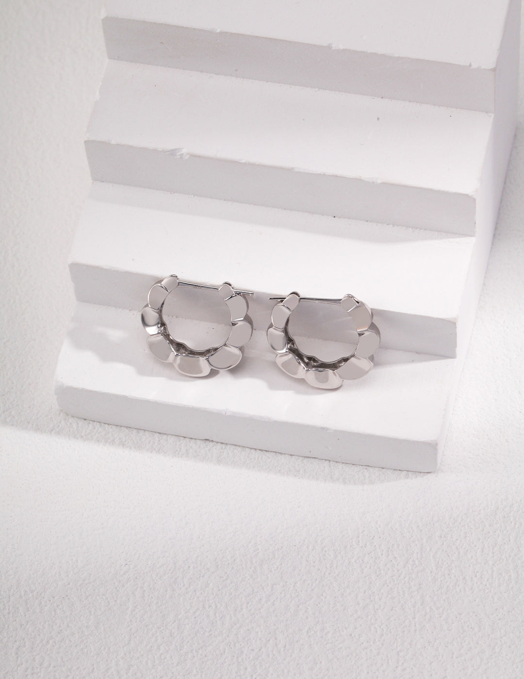 Shiny silver hoops featuring a delicate floral pattern.