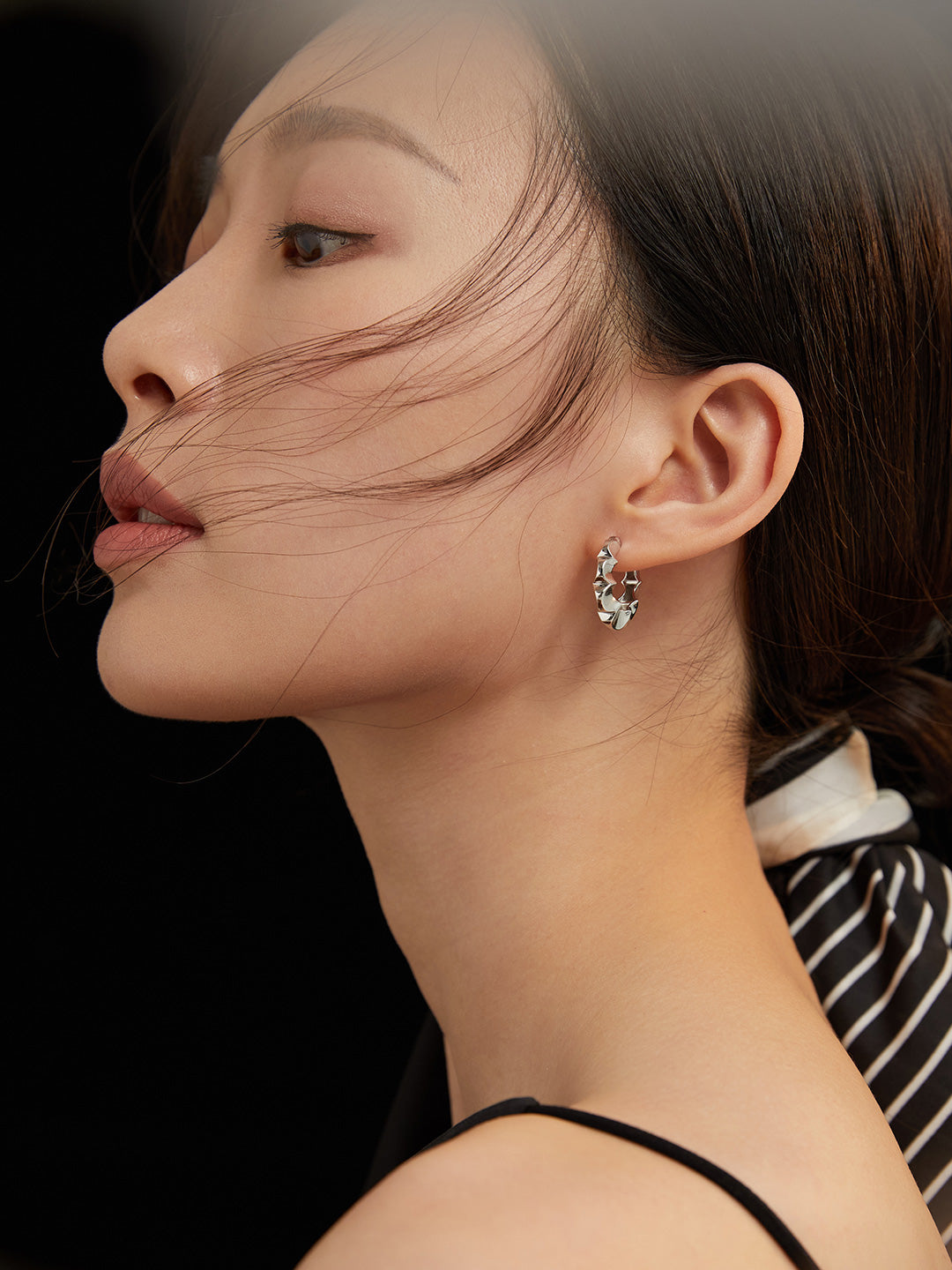 Model showcasing elegant silver floral hoop earrings on dark backdrop.