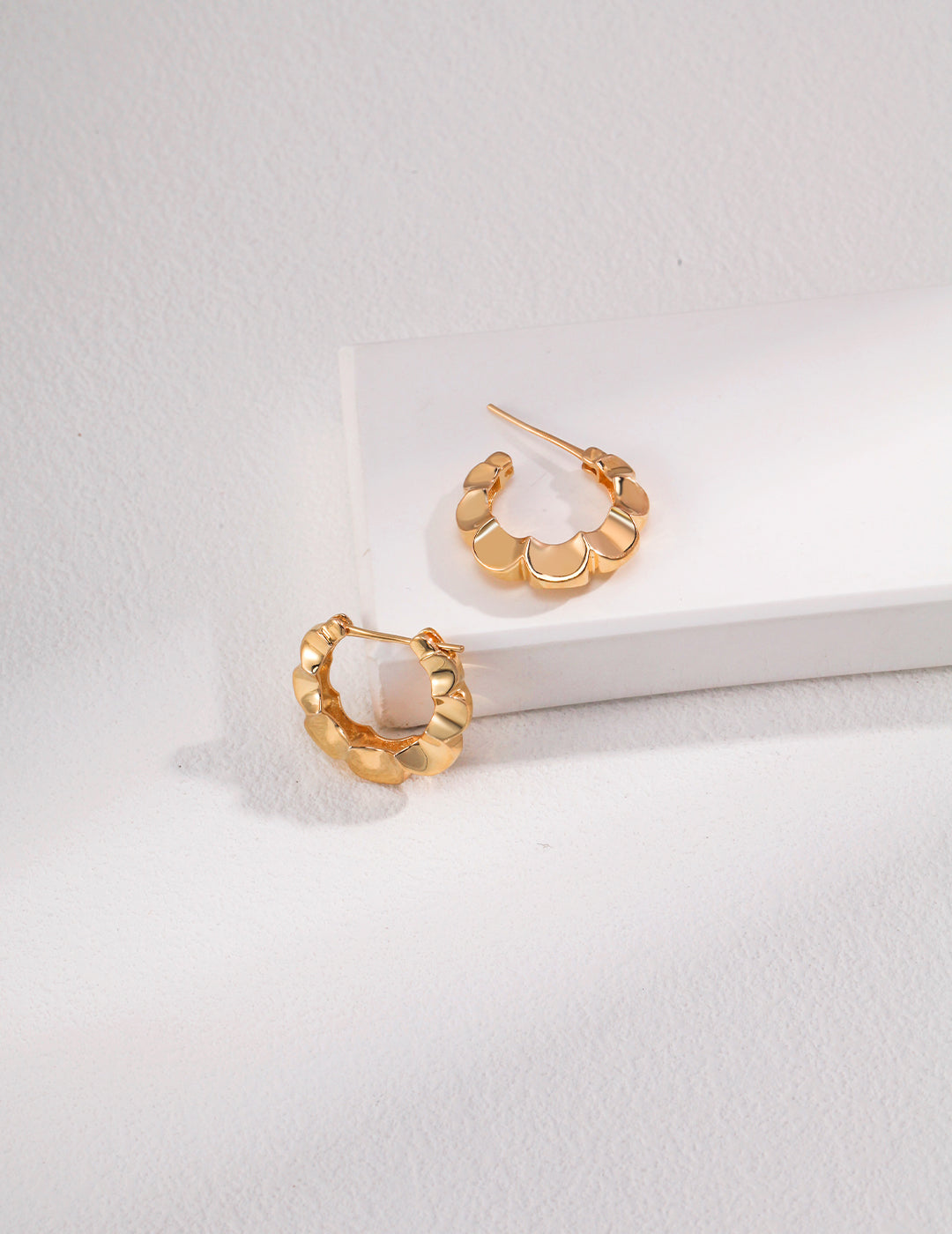 Elegant gold hoop earrings with a floral design on a white background.