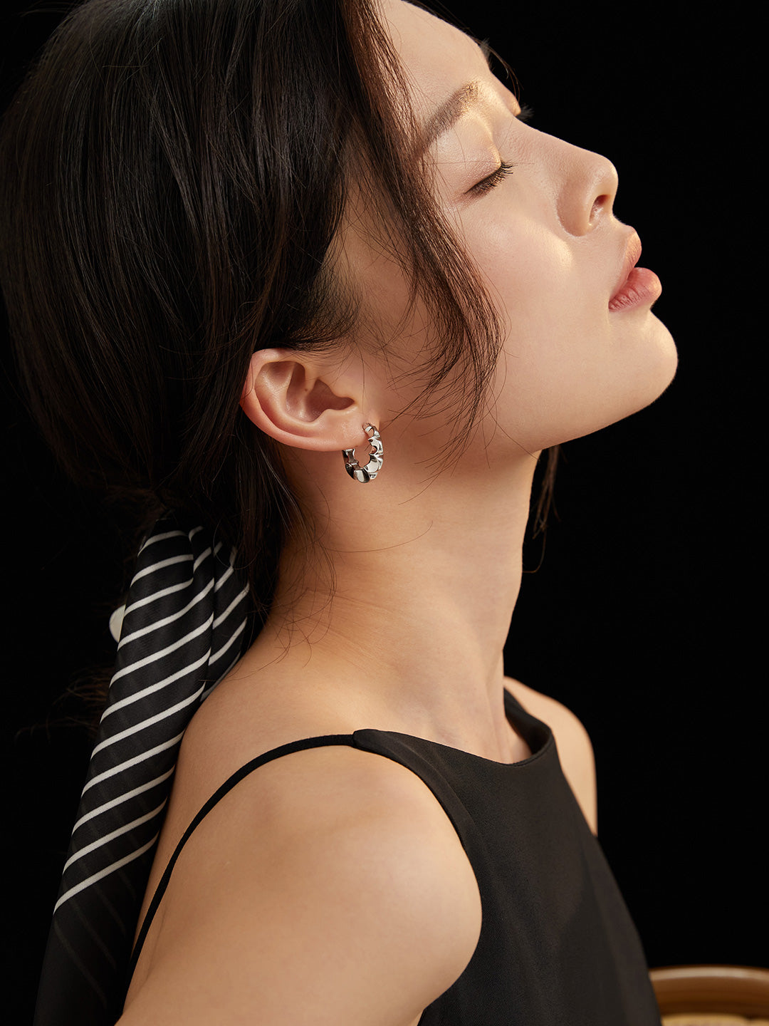 Fashionable woman donning a black top and elegant silver floral hoop earrings.