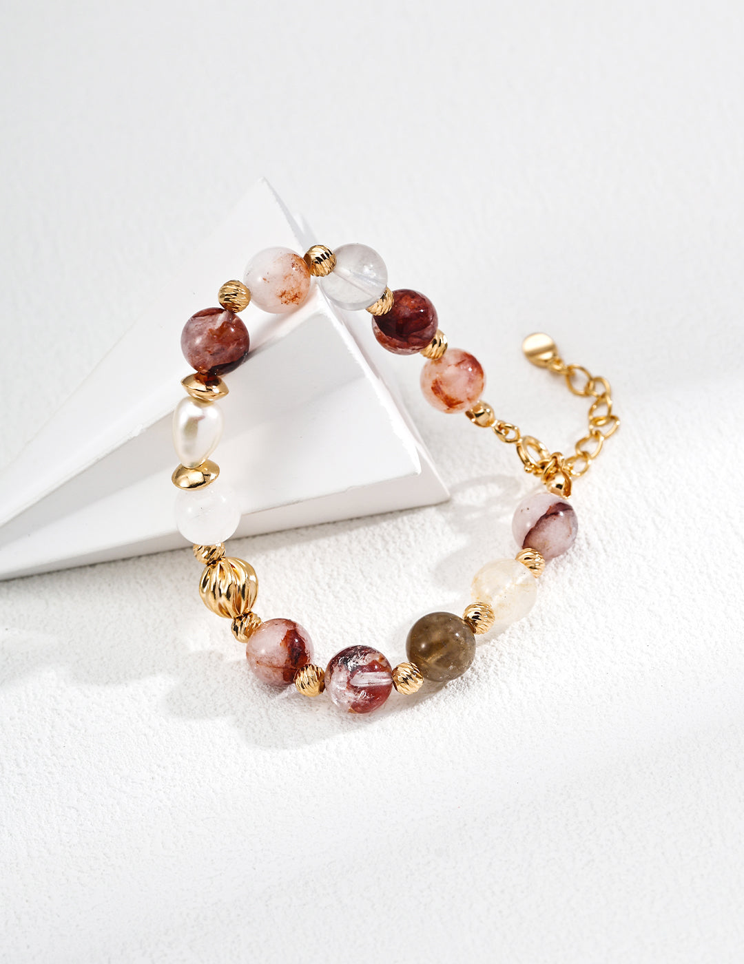 Gold chain bracelet featuring faceted beads, freshwater pearls, and resin crystal on a white background.
