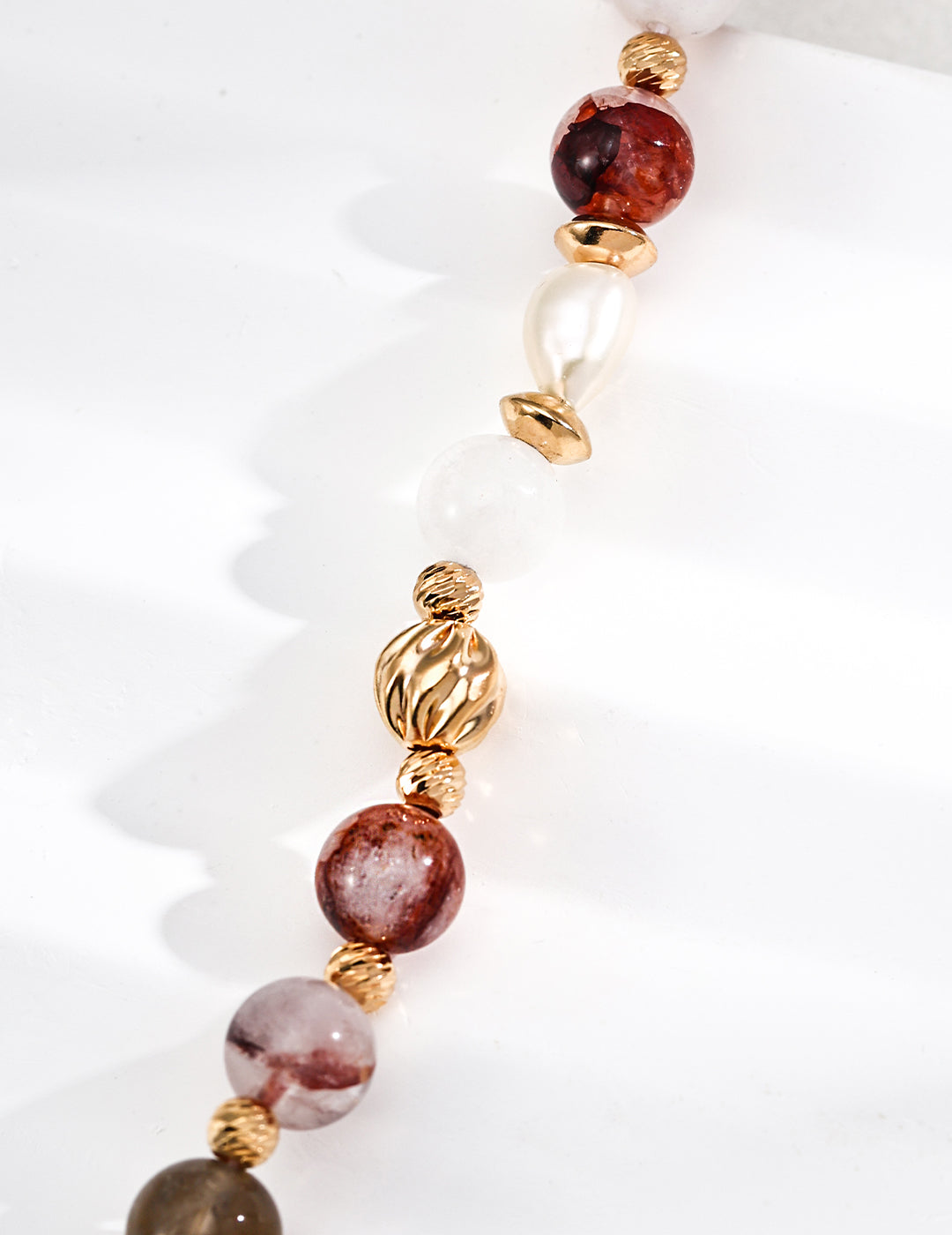 Detailed view of a necklace with gold and white stones, including faceted beads and freshwater pearls, set against a white backdrop.