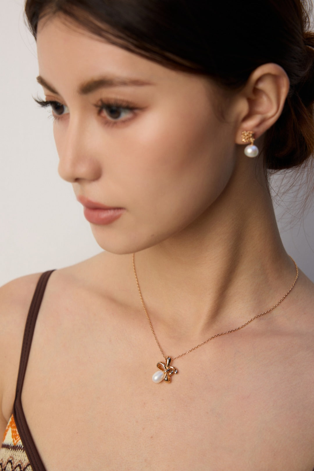 A woman displays a playful twist knot gold necklace and earrings, adding a touch of elegance to her outfit.