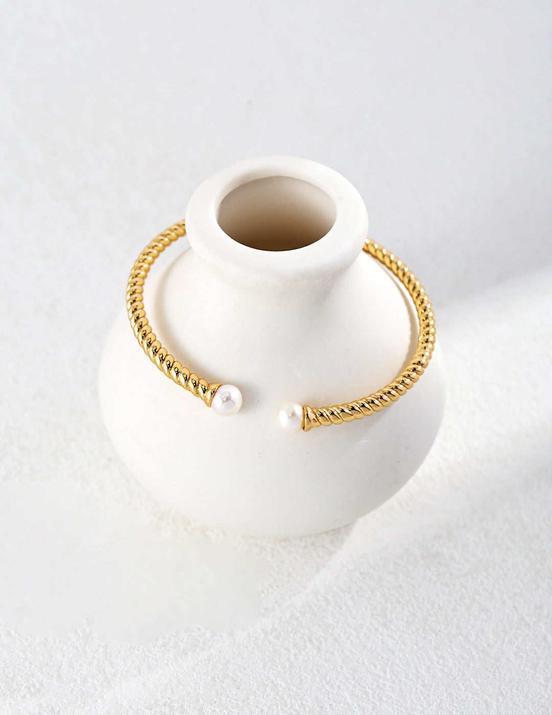 Gold twisted bangle pearls resting on a white vase.