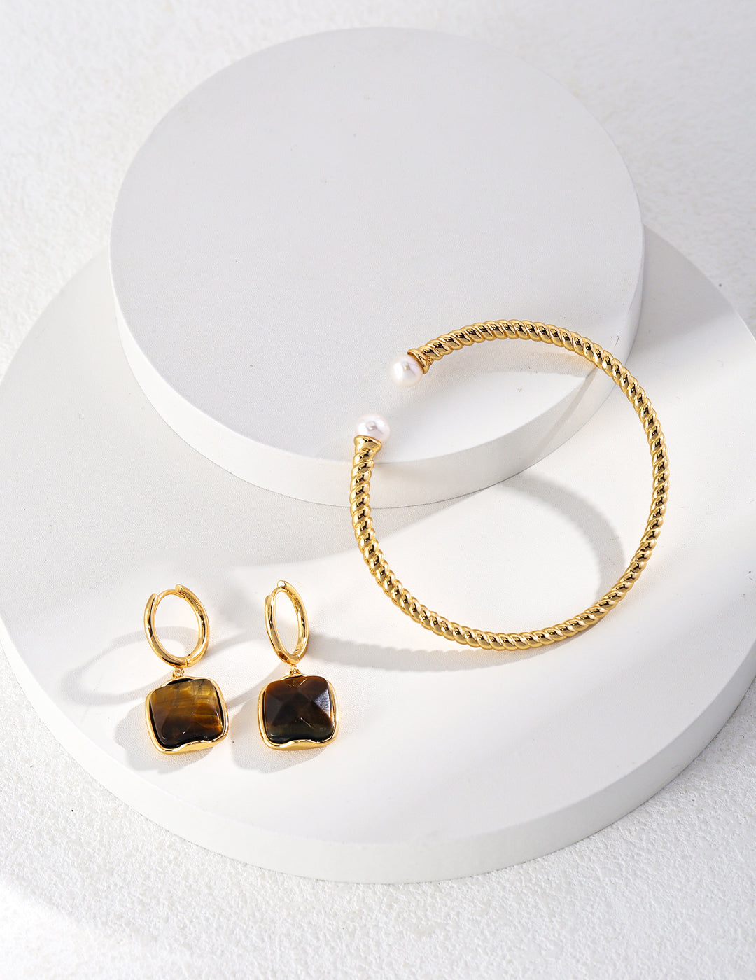 A gold twisted bangle with pearls and matching earrings on a white surface. Elegant jewelry set.