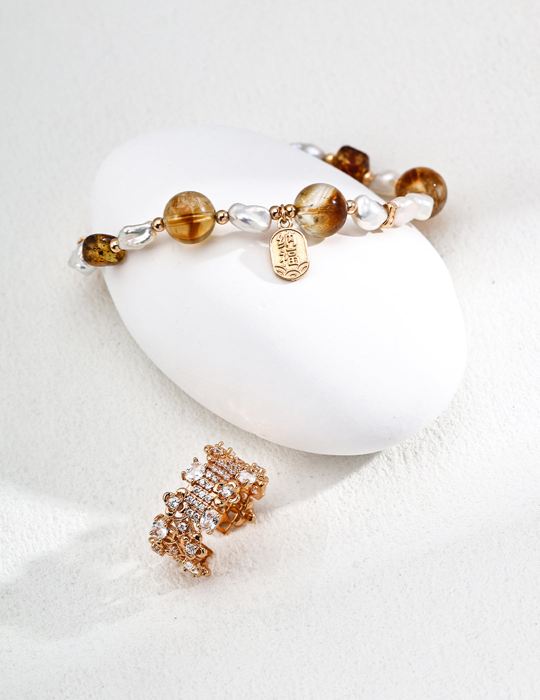 A close-up of a tiger's eye and pearl bracelet alongside a matching ring on a white surface.