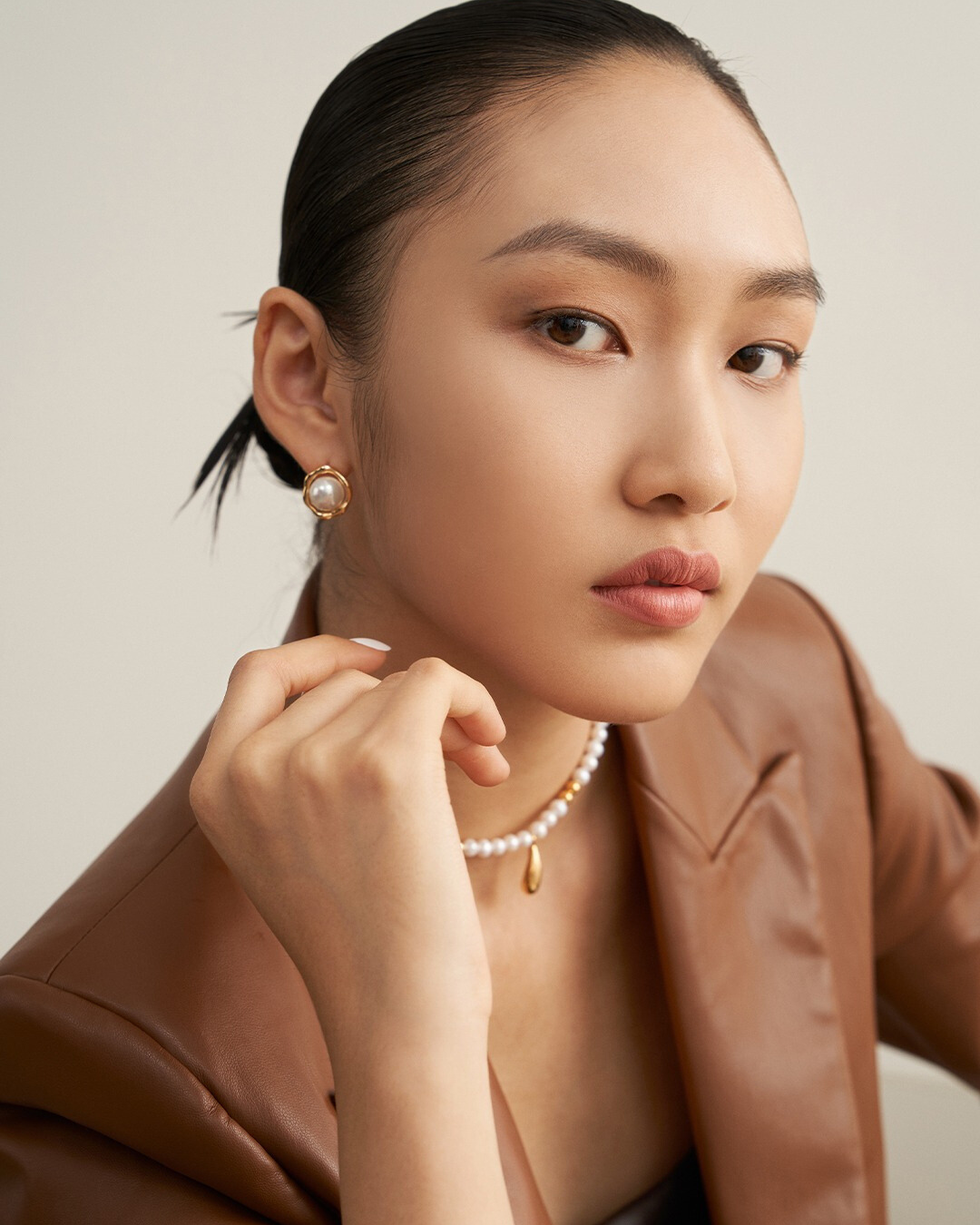 Model wearing a brown jacket and pearl necklace, accentuated by sunny side up earrings, exudes style and confidence.