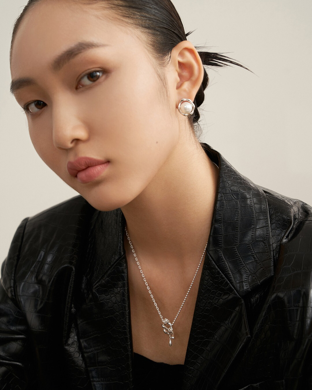 A woman in a black jacket and necklace, showcasing sunny side up earrings, poses confidently as a model.