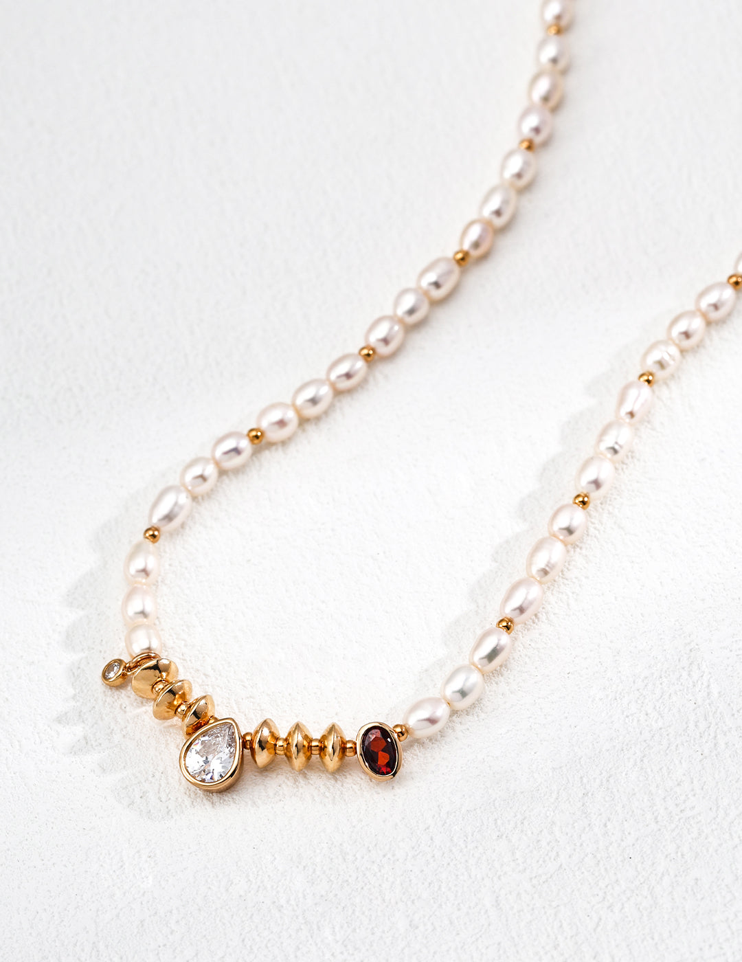 Luxurious pearl necklace with gold chain, showcasing a teardrop red stone and cubic zirconia for an elegant touch.