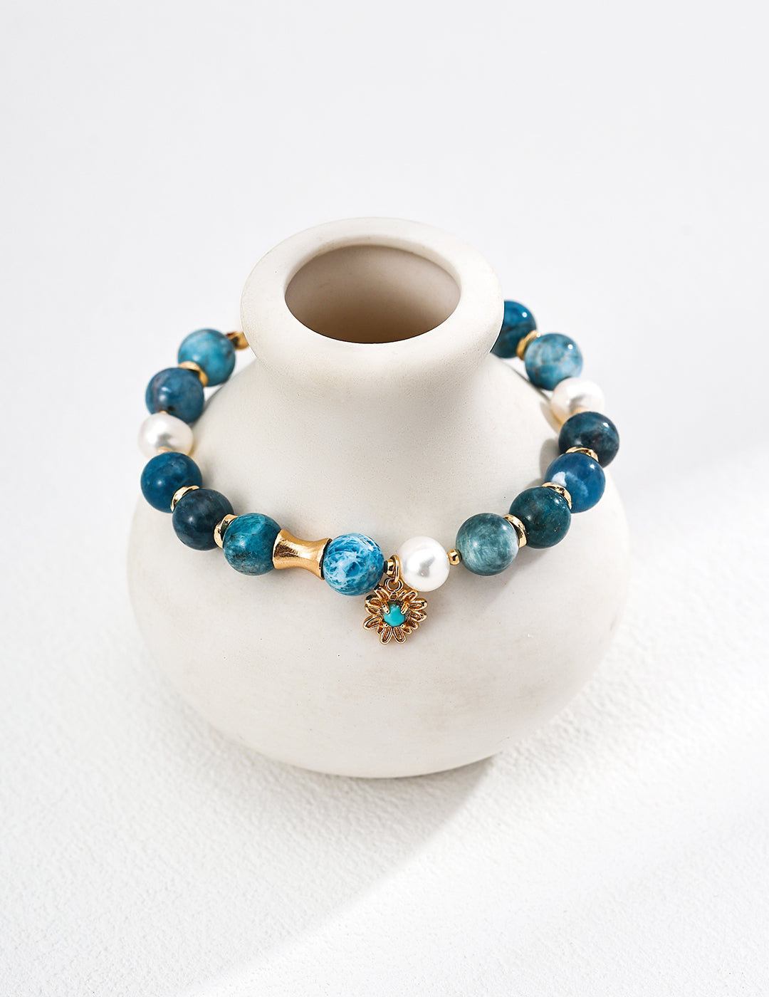 Elegant blue stone bracelet with gold accents, made of azurite, freshwater pearls, and turquoise against a ceramic white vase.