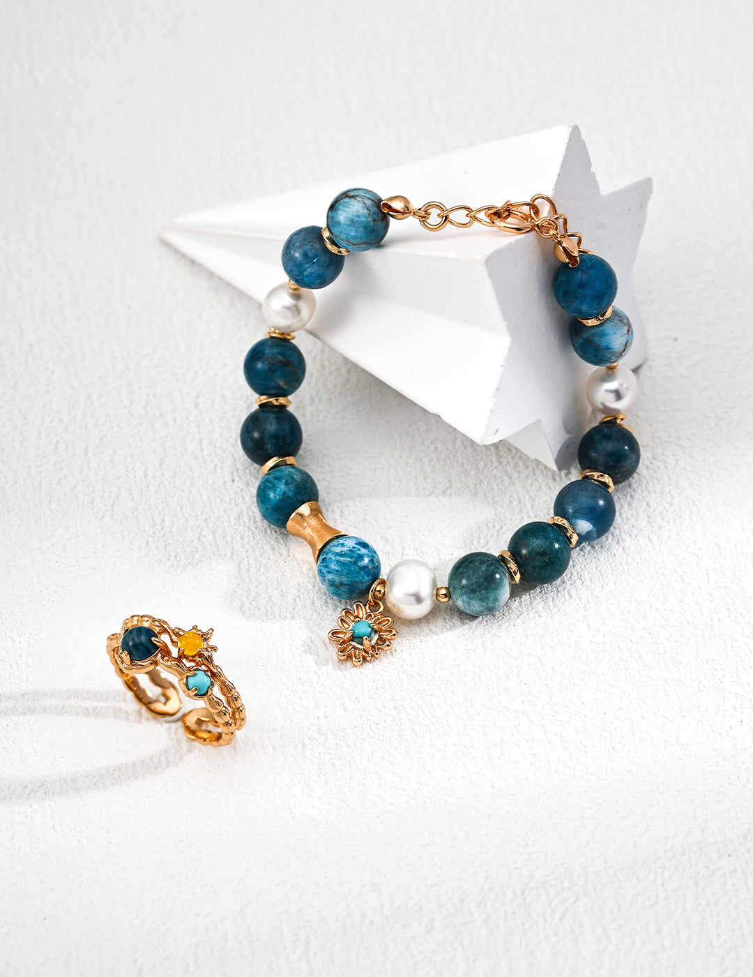 A blue stone bracelet made of azurite, freshwater pearls, and turquoise, paired with a gold ring on a white surface.