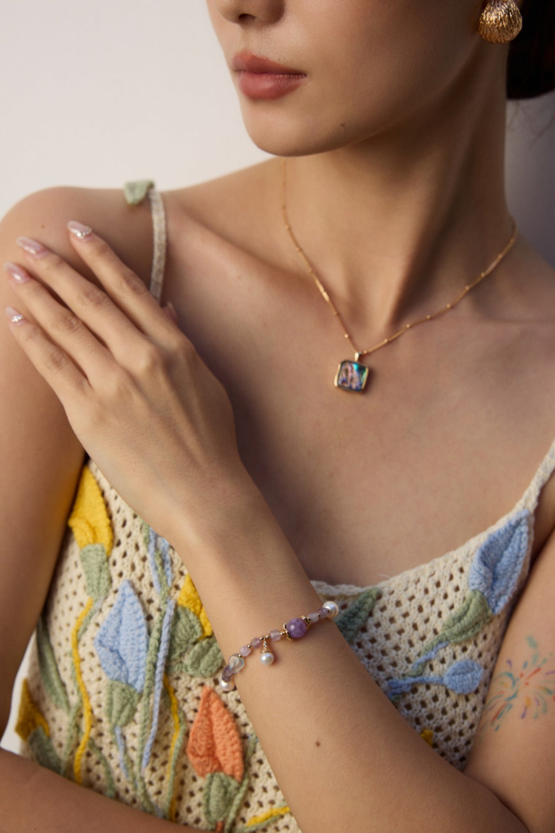 A woman showcases a necklace and bracelet adorned with a flower, made of amethyst and icy aquamarine stones.