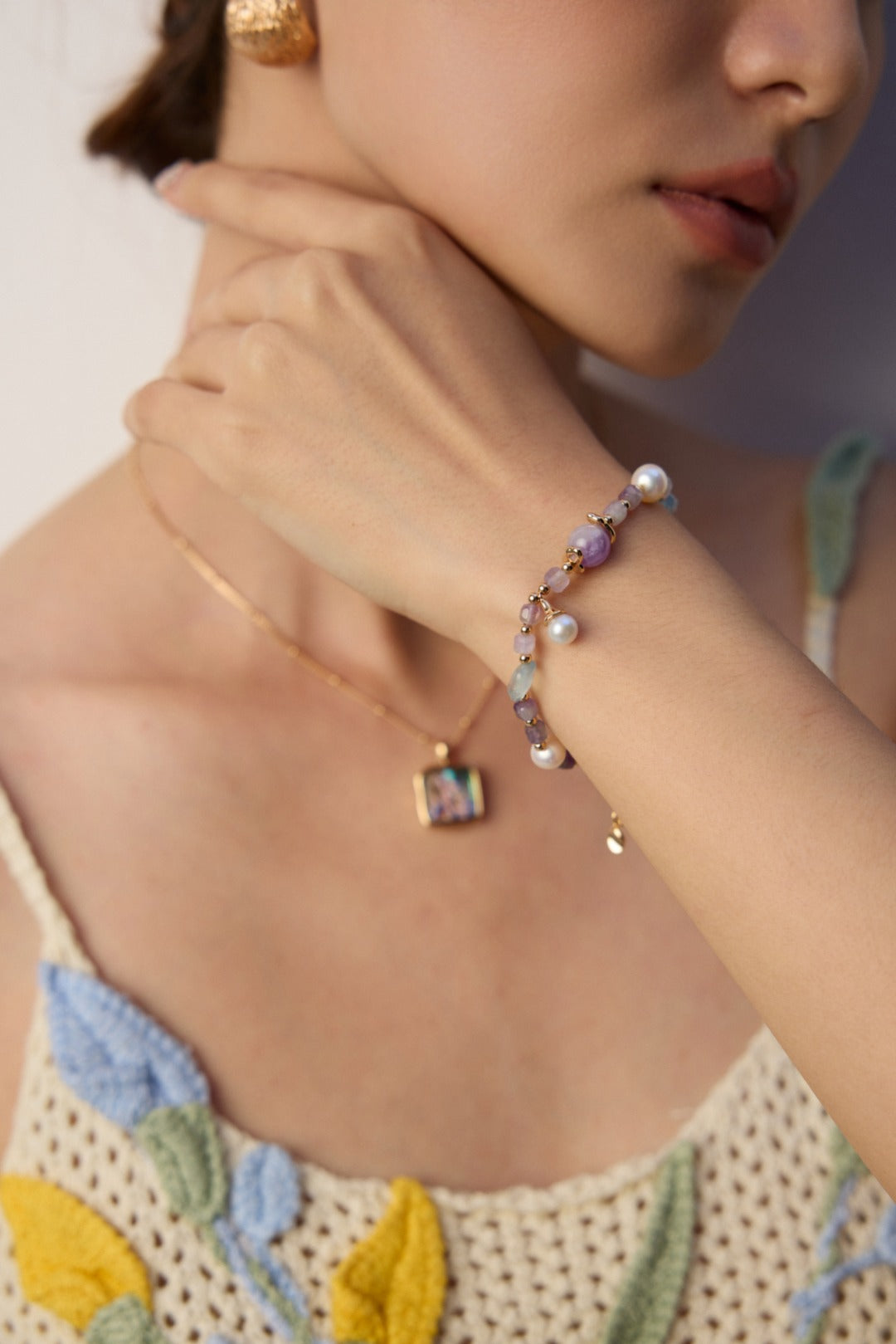 A woman wearing a bracelet and necklace featuring amethyst and icy aquamarine gemstones.