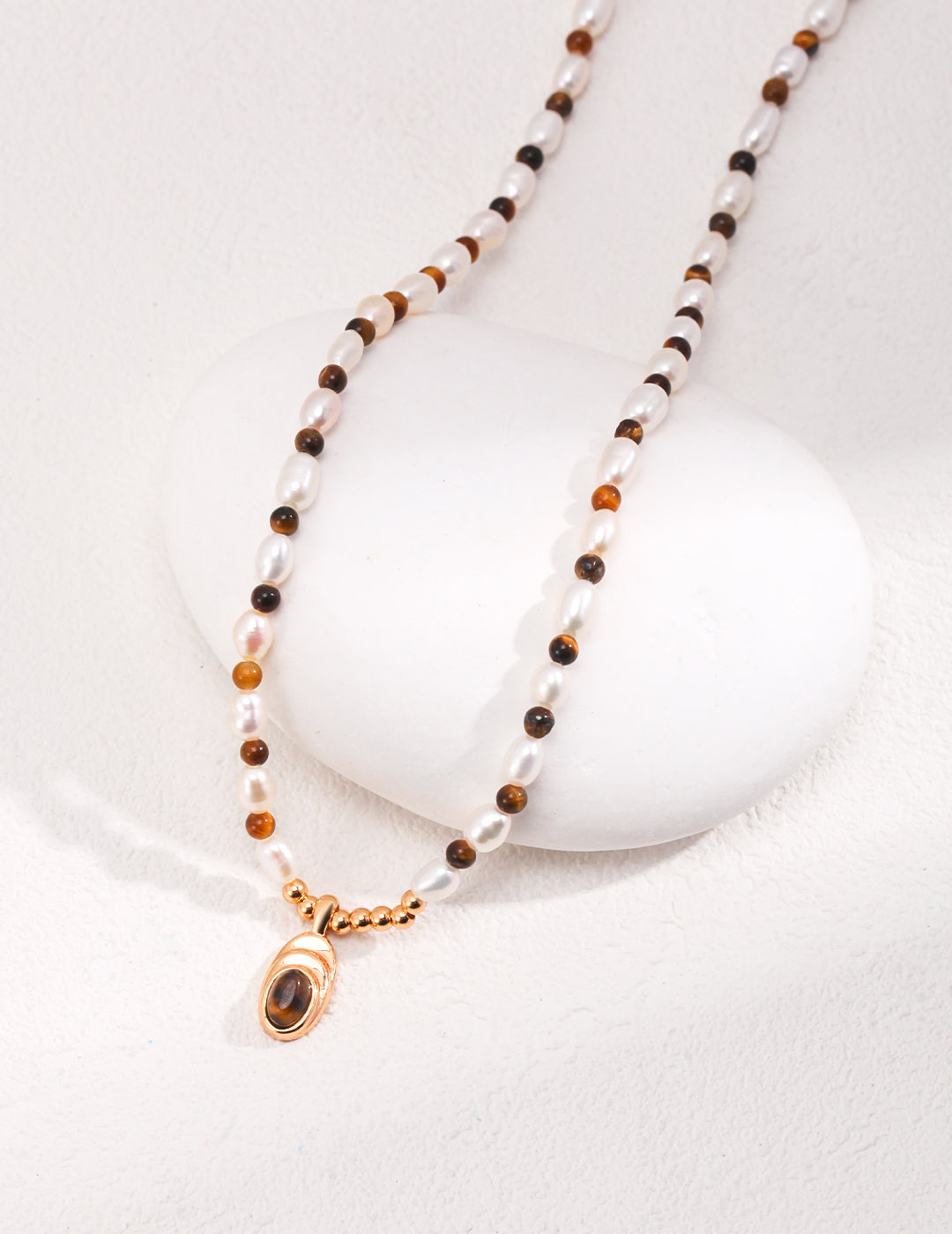 Stylish necklace adorned with gold pendant, black and white stone, tiger's eye beads, and freshwater pearl beads.