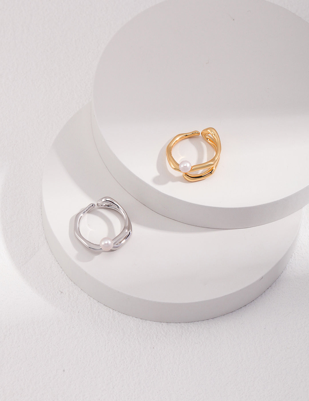 Two unique silver and gold rings with freshwater pearl, elegantly displayed on a white surface.