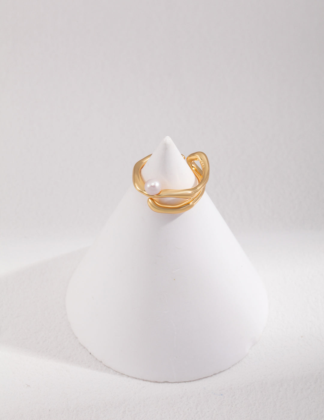 A unique gold ring with a freshwater pearl, elegantly placed on top of a white cone.