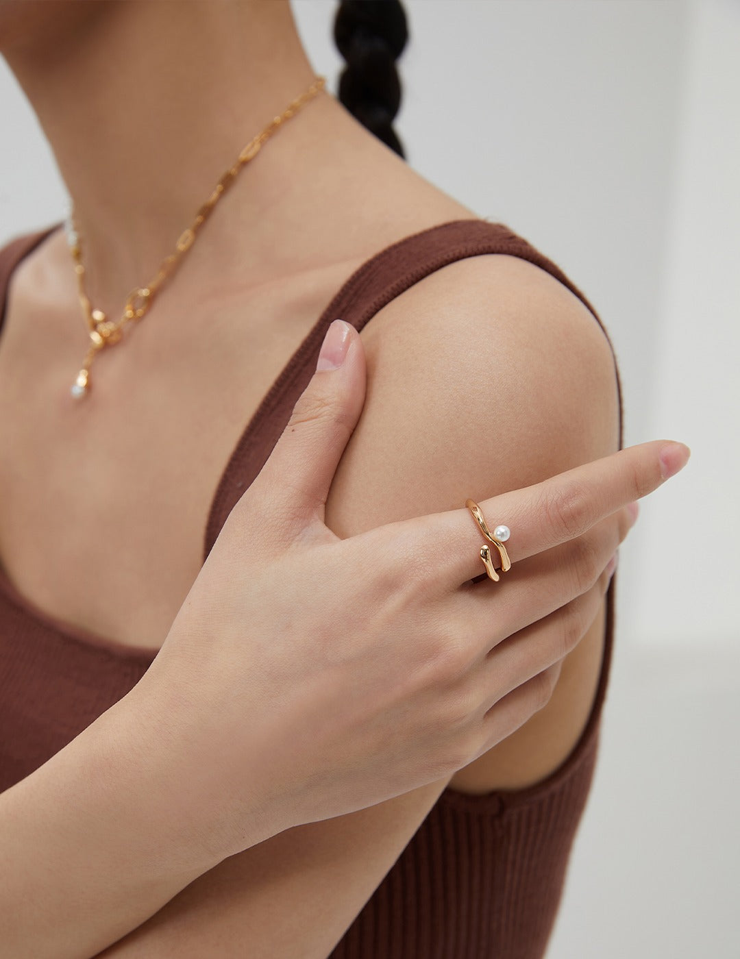 A woman showcasing a unique gold ring with a freshwater pearl pendant, complemented by a matching necklace.