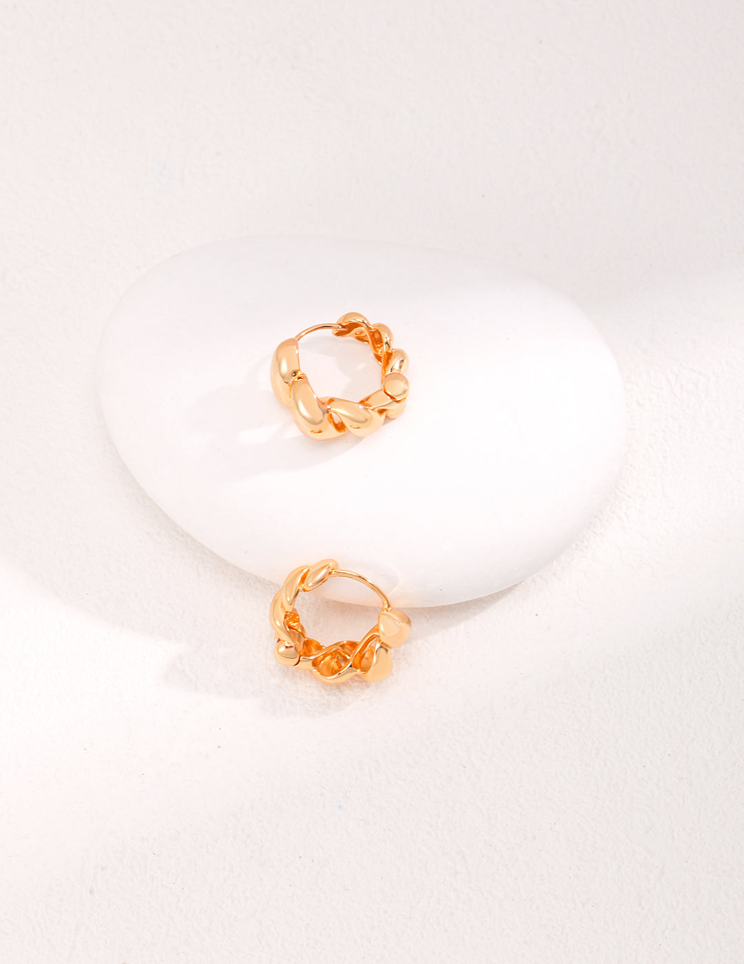 A pair of gold hoops gracefully positioned on a white stone.