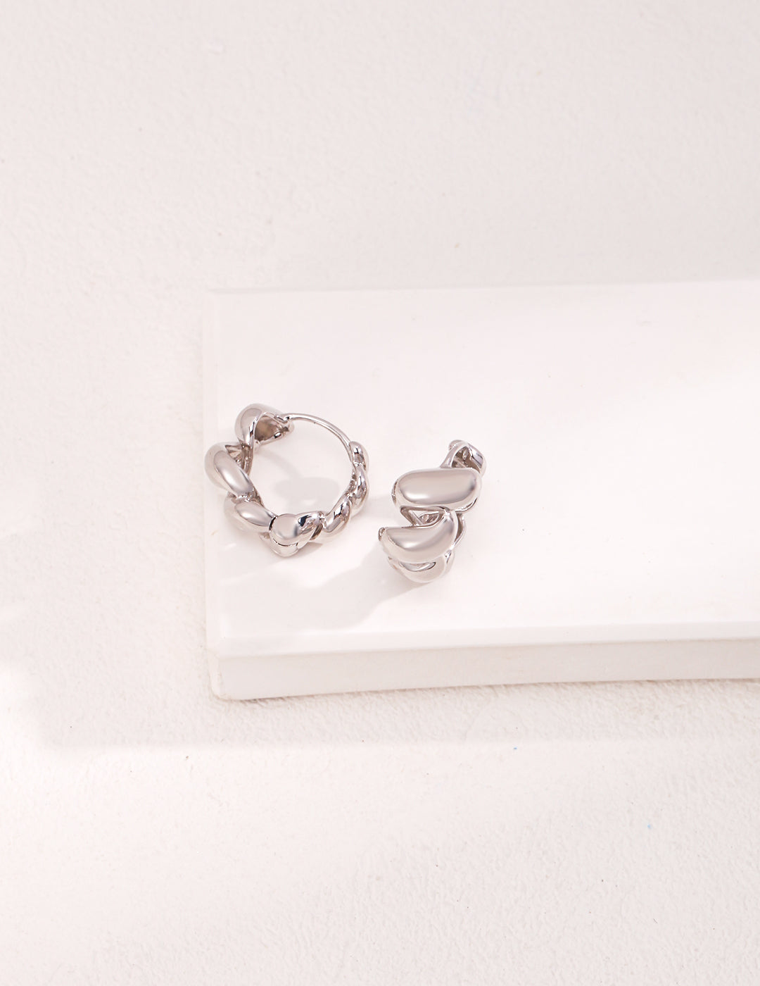 Two silver hoops resting on a white surface.