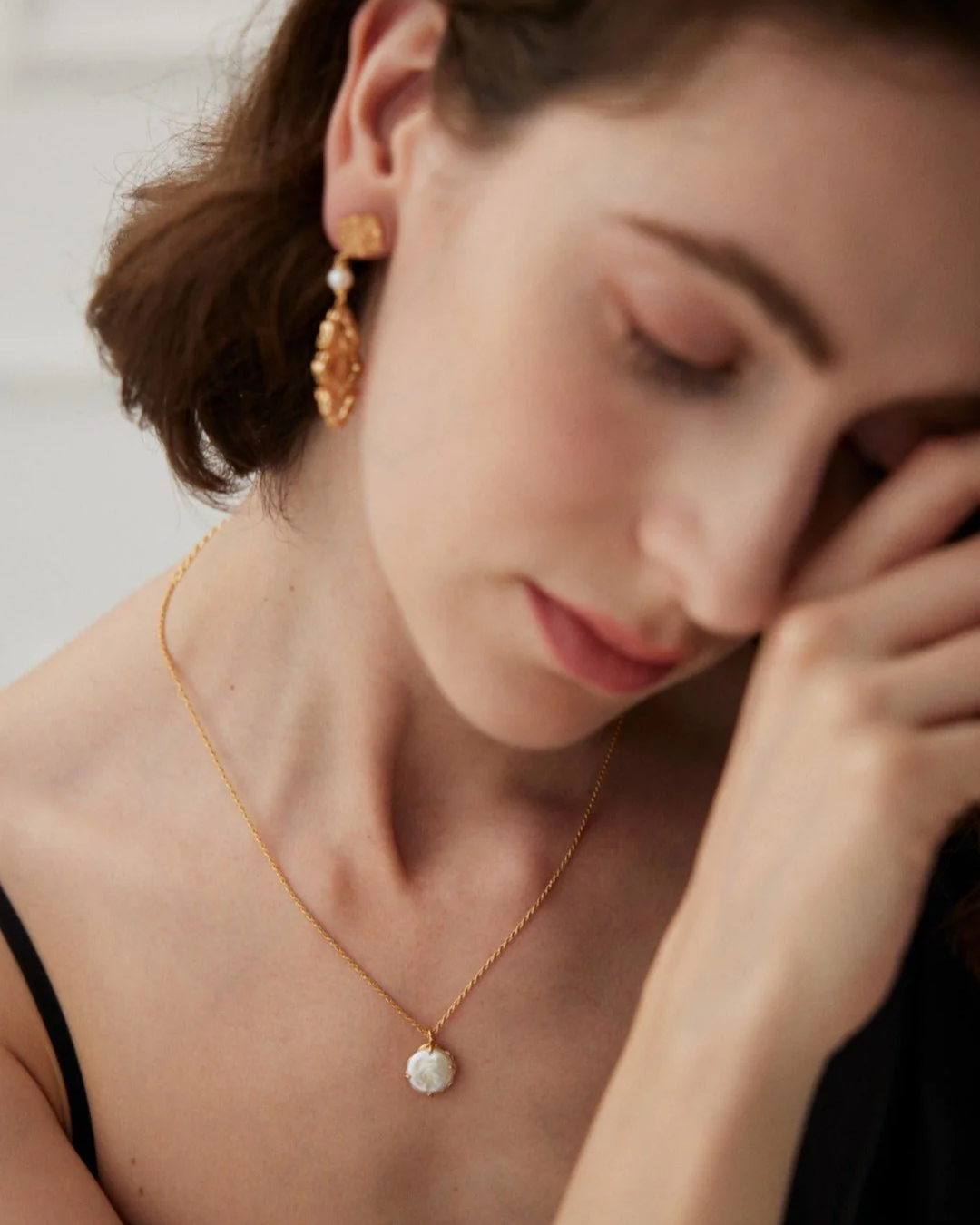 A woman models a gold necklace and earrings, featuring a reversible pearl necklace that can be worn in two styles.