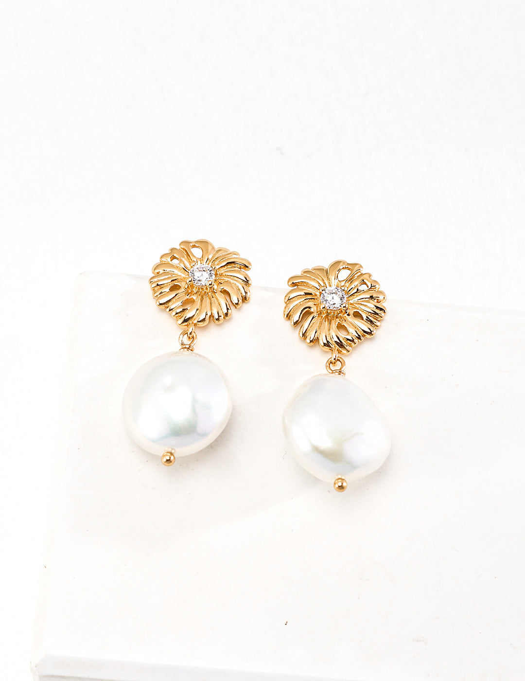 Gold plated pearl daisy earrings on white surface.