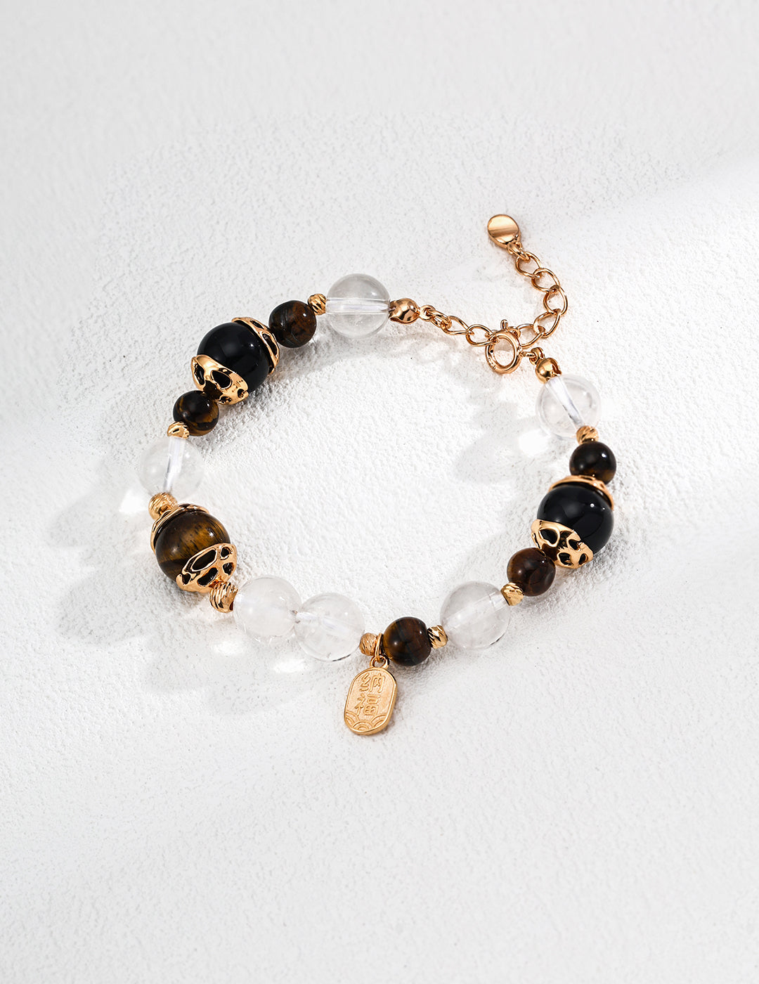 A stylish bracelet made of black agate and Tiger's eye beads, clear crystals, gold accents, and a small pendant, resting on a white background.