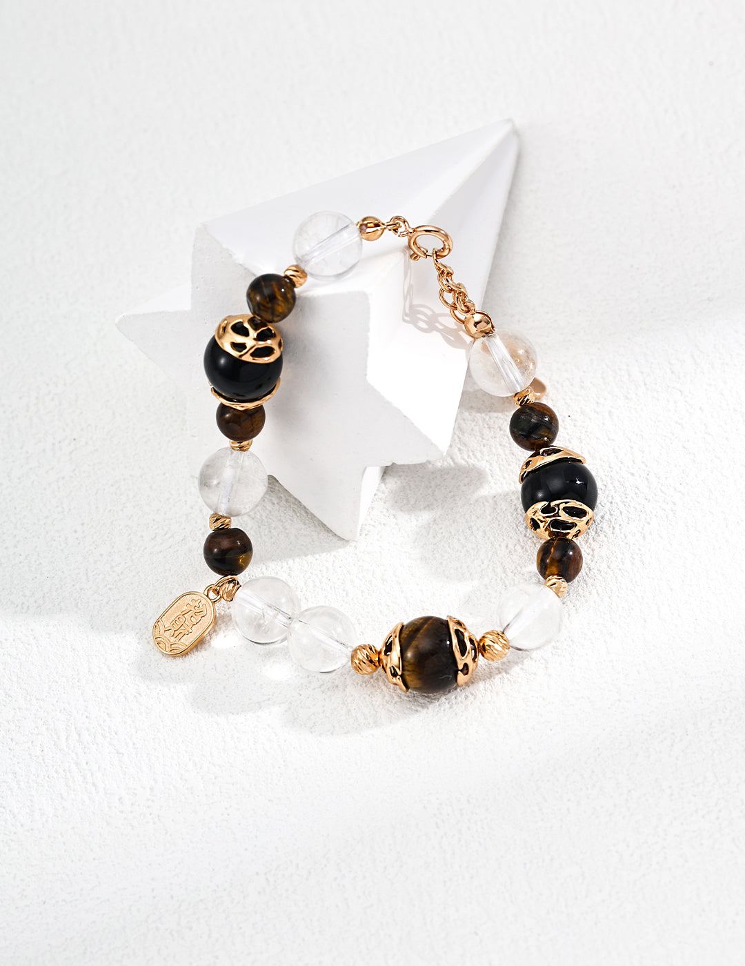 Elegant bracelet featuring black agate and tiger eye beads, clear crystals, and gold-toned accents, displayed on a white star sculpture.