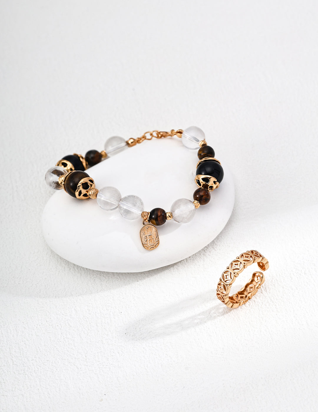 A stylish bracelet with clear and black beads, alongside a delicate gold ring, resting on a smooth surface.