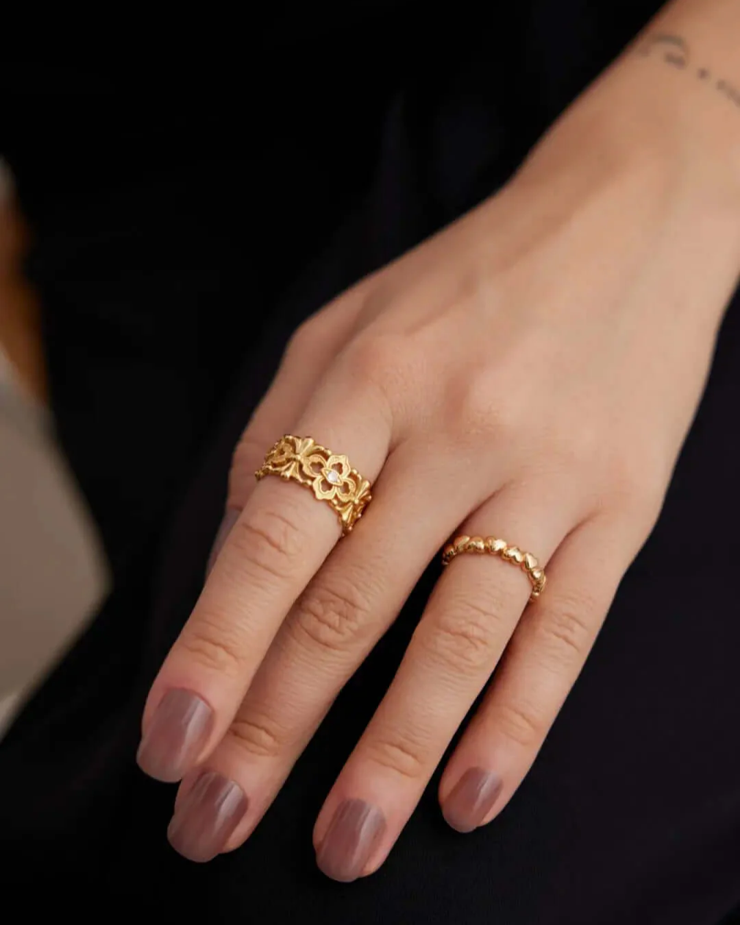 A woman's hand featuring a gold ring, elegantly stacked with other rings.