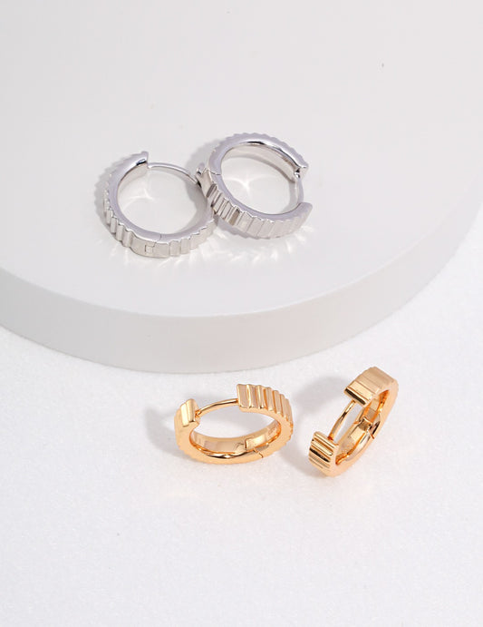 Two pairs of gearwheel inspired hoop earrings, one gold and one silver, placed on a white surface.