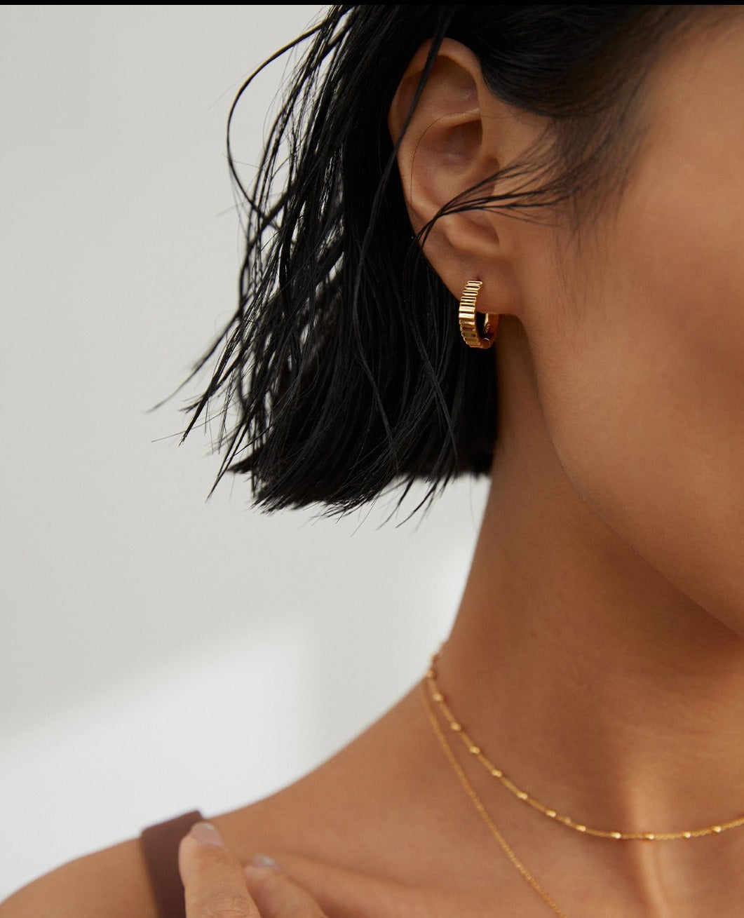 Close-up of model wearing gold chain and hoop earring.