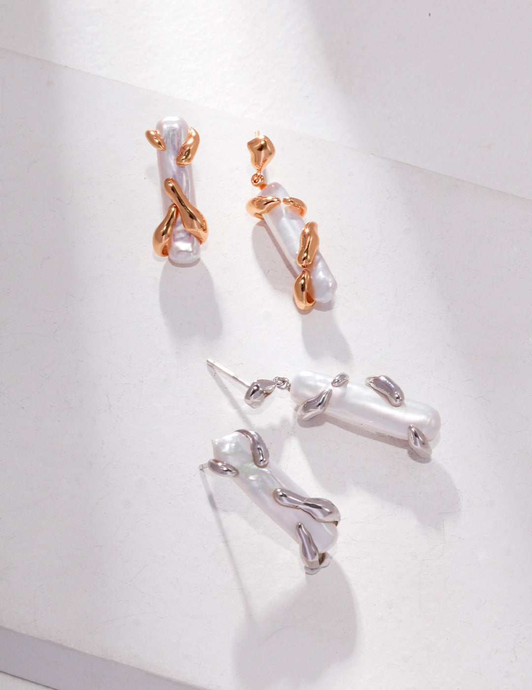 Two pairs of earrings: asymmetric pearls, silver, and gold, displayed on a white surface.