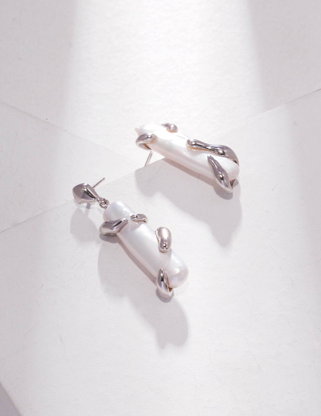 Stylish silver asymmetric pearl earrings on white surface.