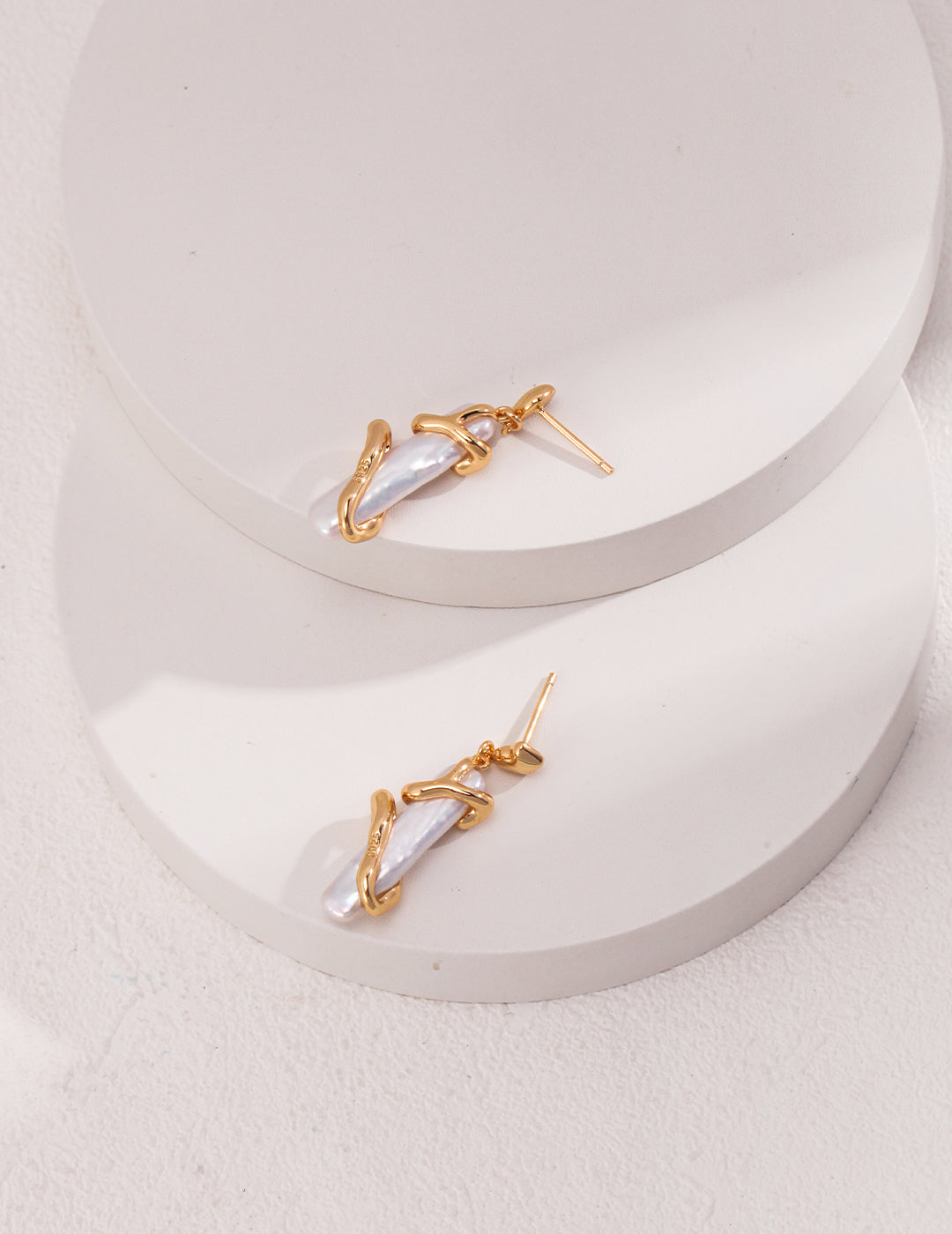 Two elegant gold and white earrings with symmetric pearls, resting on a pristine white surface.