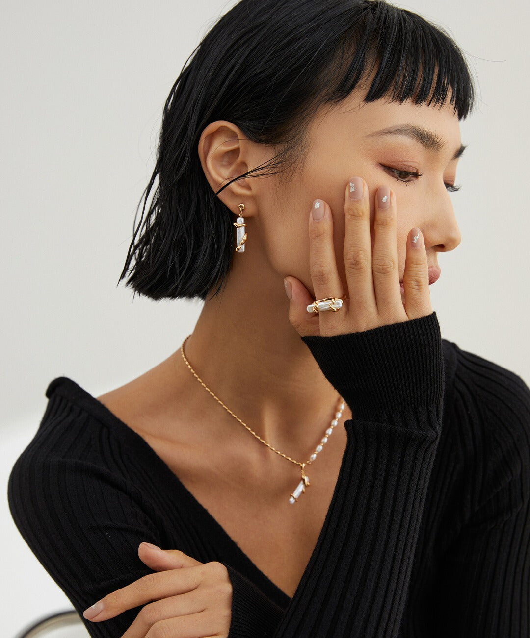 A stylish woman in a black sweater and gold baroque pearls necklace, showcasing her elegant fashion sense and accessorizing skills.