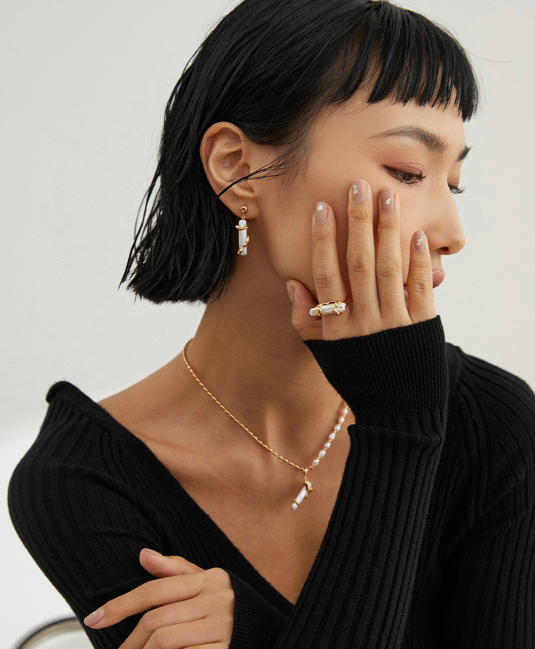 A stylish woman in a black sweater and jewelry, including a gold plated freshwater pearl ring.