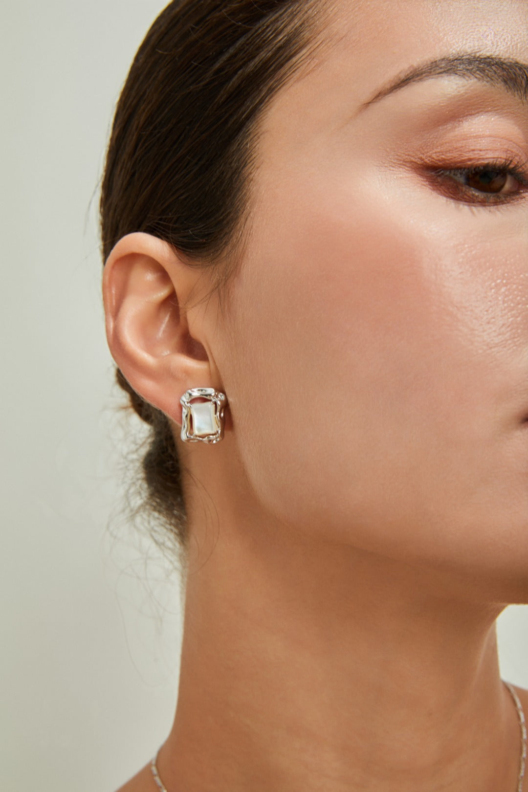 Close-up of a woman wearing chic earrings adorned with brilliant square shell pearl studs, emphasizing her refined taste.