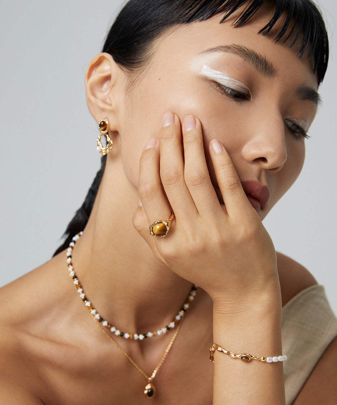 Woman wearing gold and pearl necklace, matching gold bracelet with freshwater pearls and tiger's eye centerpiece.