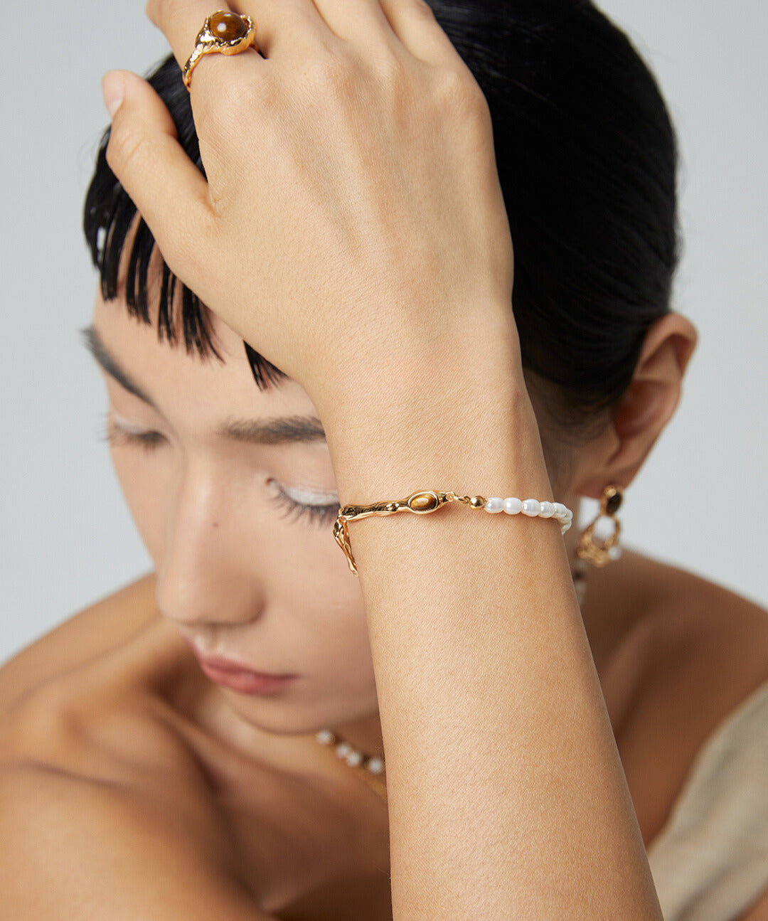 A model showcasing a stunning gold bangle with a pearl bracelet, adorned with freshwater pearls and a tiger's eye centerpiece.