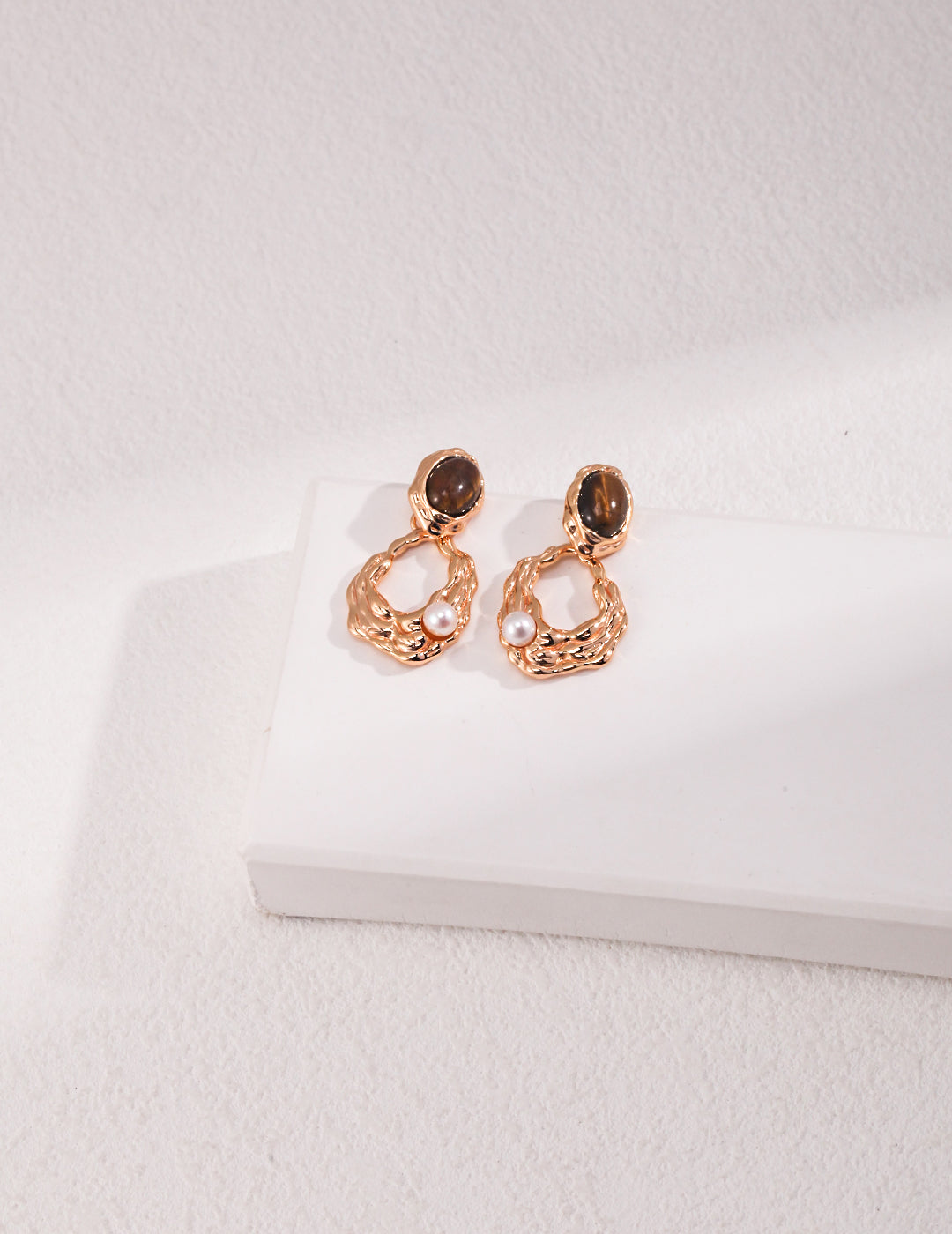 Stunning gold plated earrings featuring tiger's eye freshwater pearls, resting on a pristine white surface.