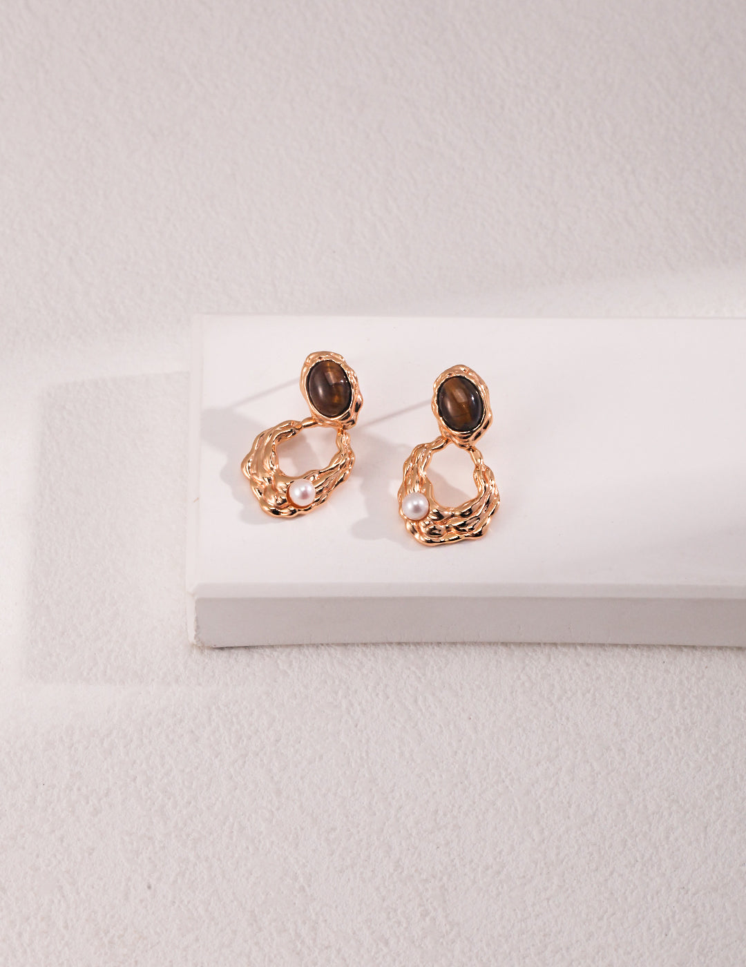 Gold plated tiger's eye freshwater pearls drop earrings on white surface.