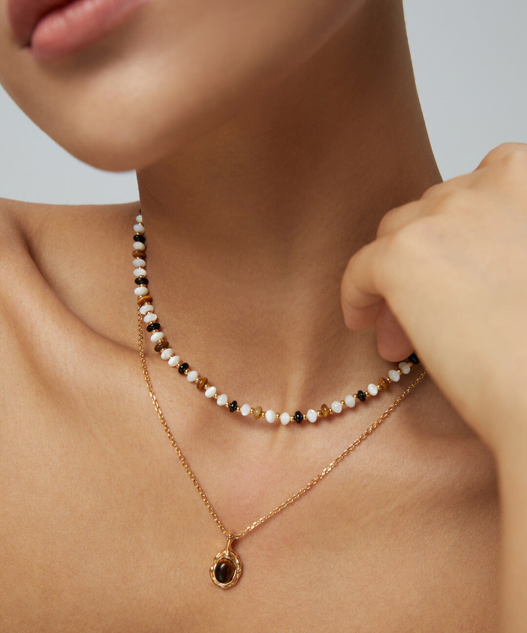 Woman in gold chain necklace with black and white pearls, featuring tiger's eye pendant.