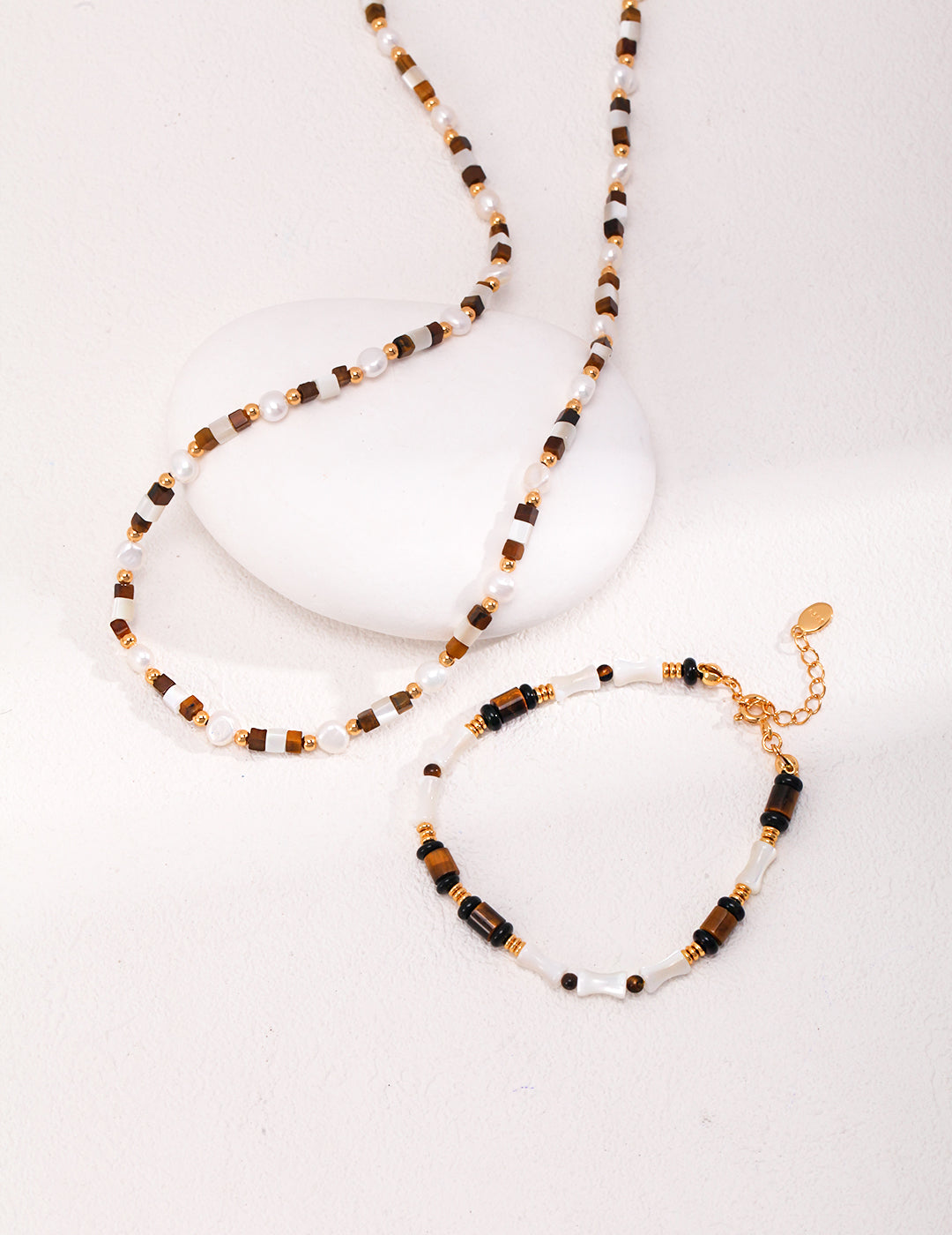 A gold plated bracelet and necklace set with a white stone, nacre, black agate, and tiger's eye.