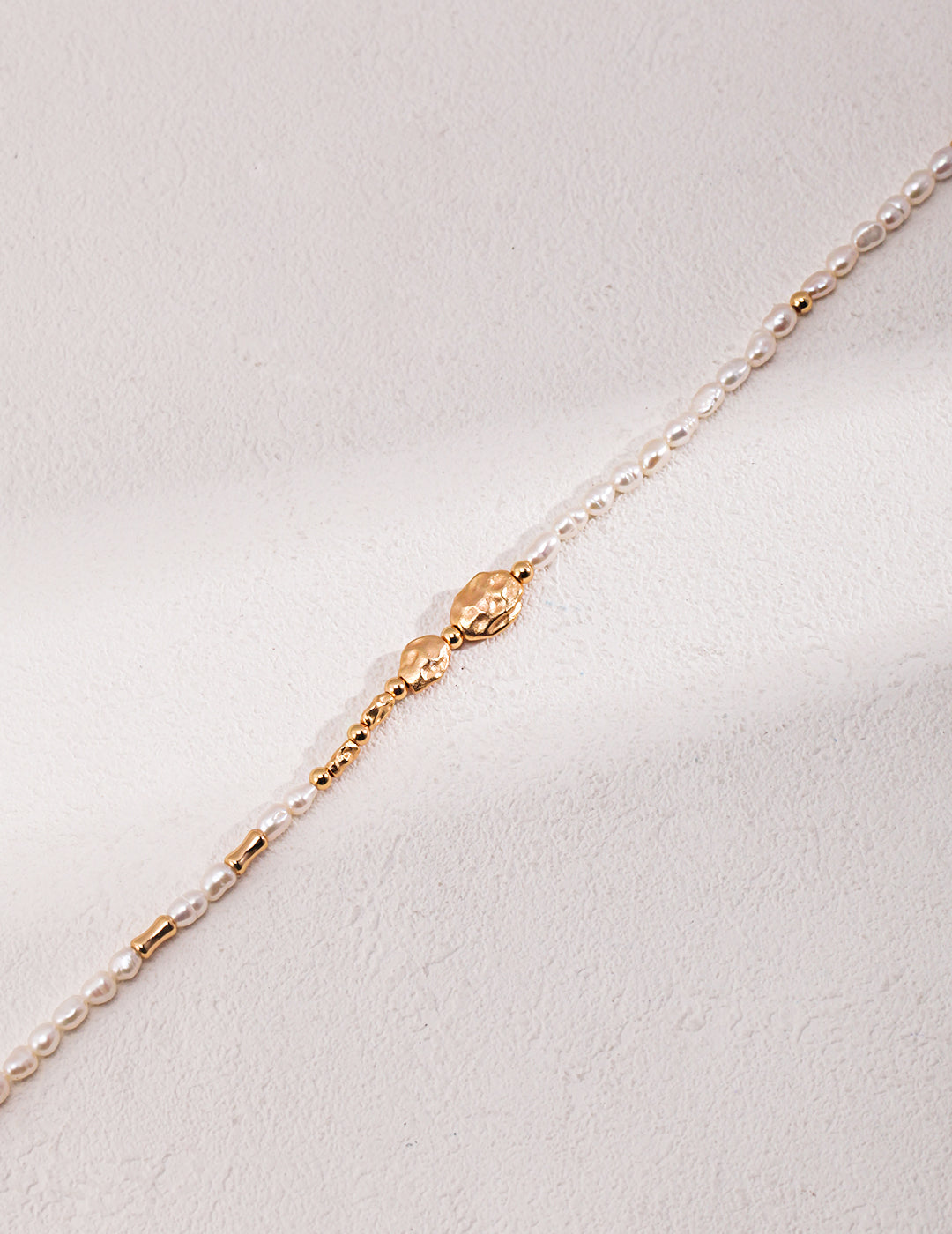 Close-up of elegant gold chain with small freshwater pearl clasp.