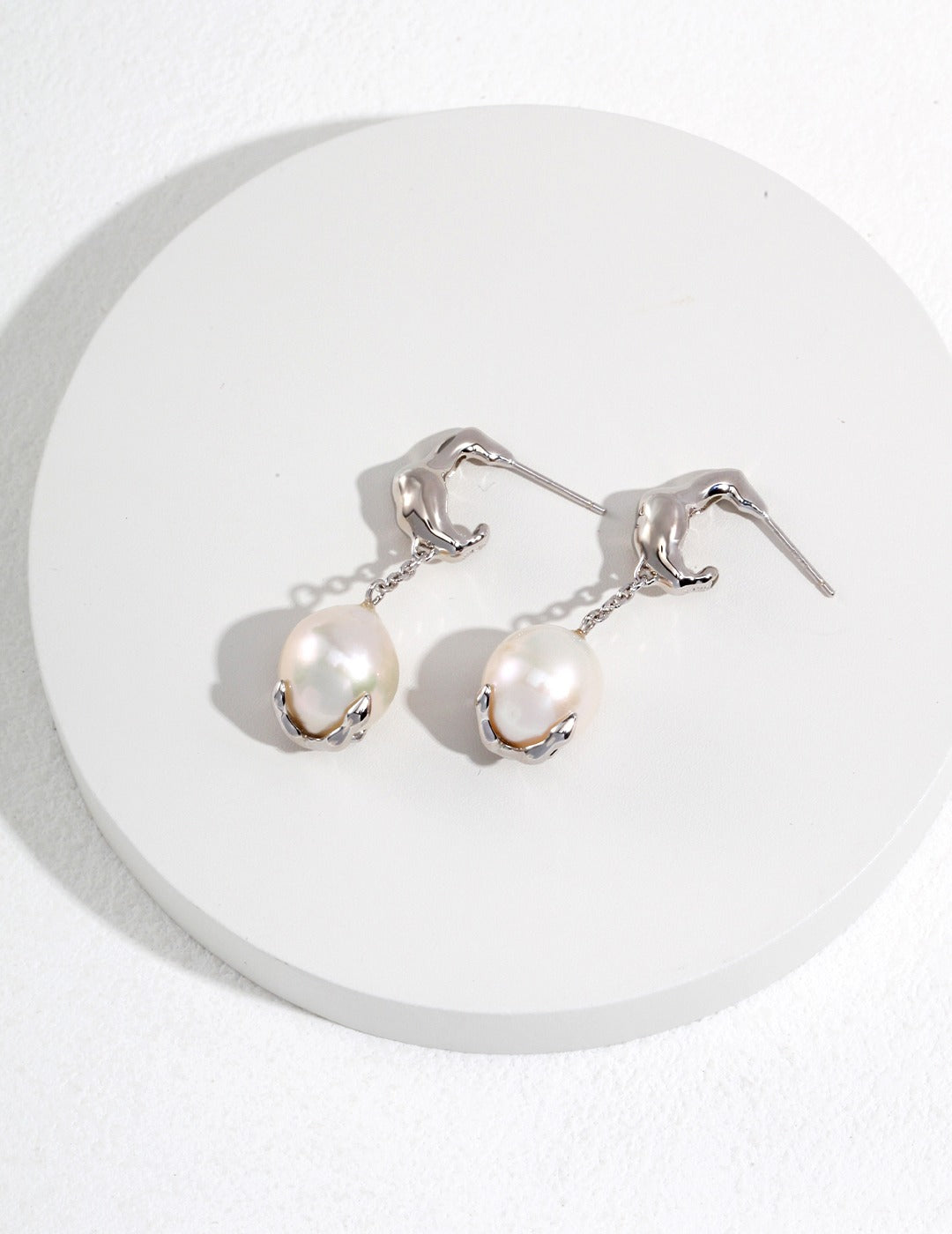 A close-up of silver pearl earrings elegantly placed on a white plate, emphasizing their shine and sophistication.