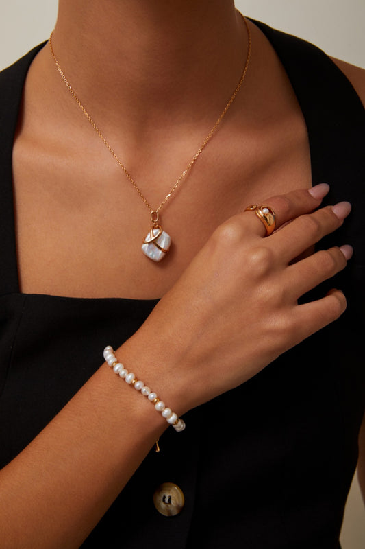 A woman adorned in a gold necklace with a baroque pearl pendant and bracelet, exuding elegance and charm for any occasion.