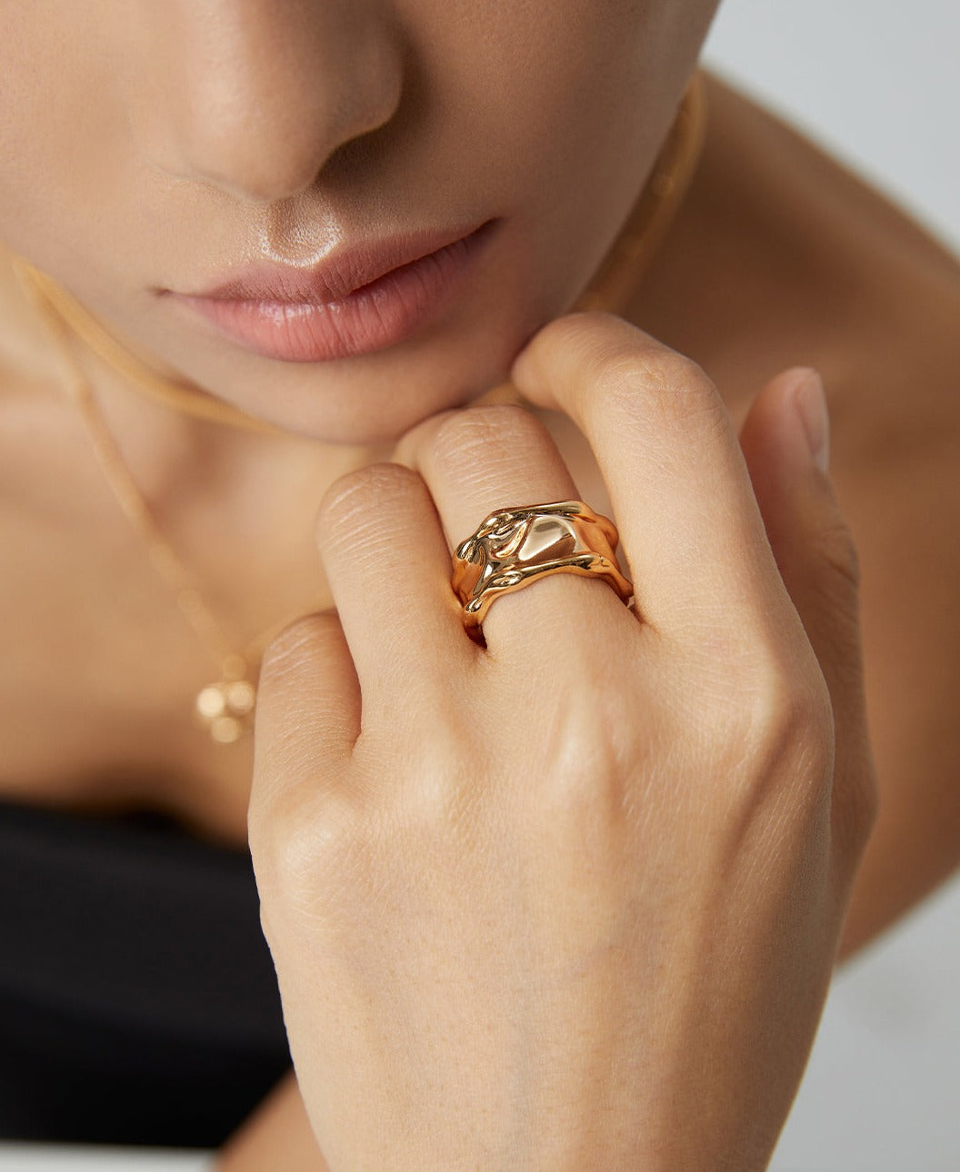 Close-up of woman's hand wearing textured wavy-patterned gold ring.