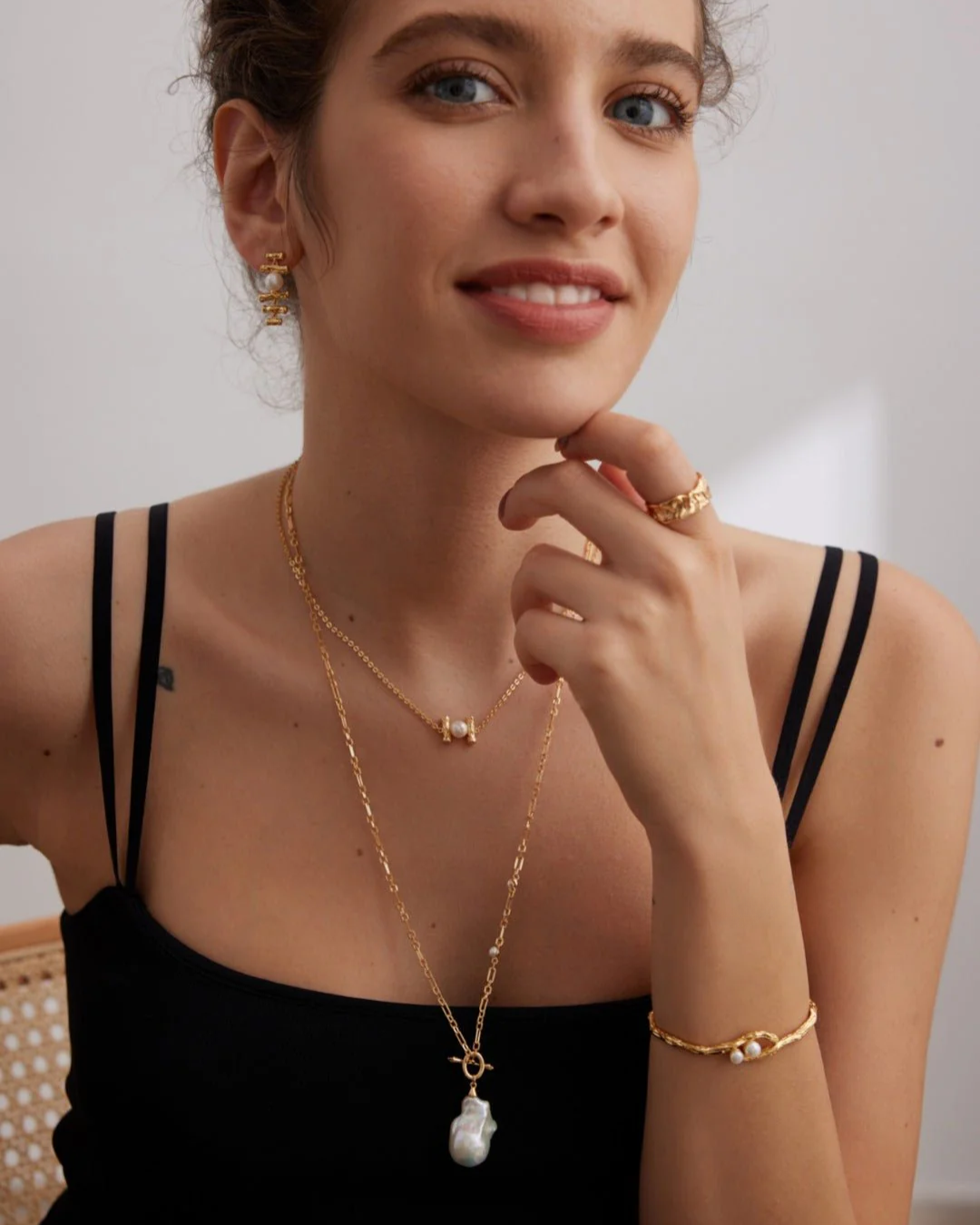 A woman displays sophistication with a gold necklace paired with a lustrous pearl necklace, embodying elegance and grace.