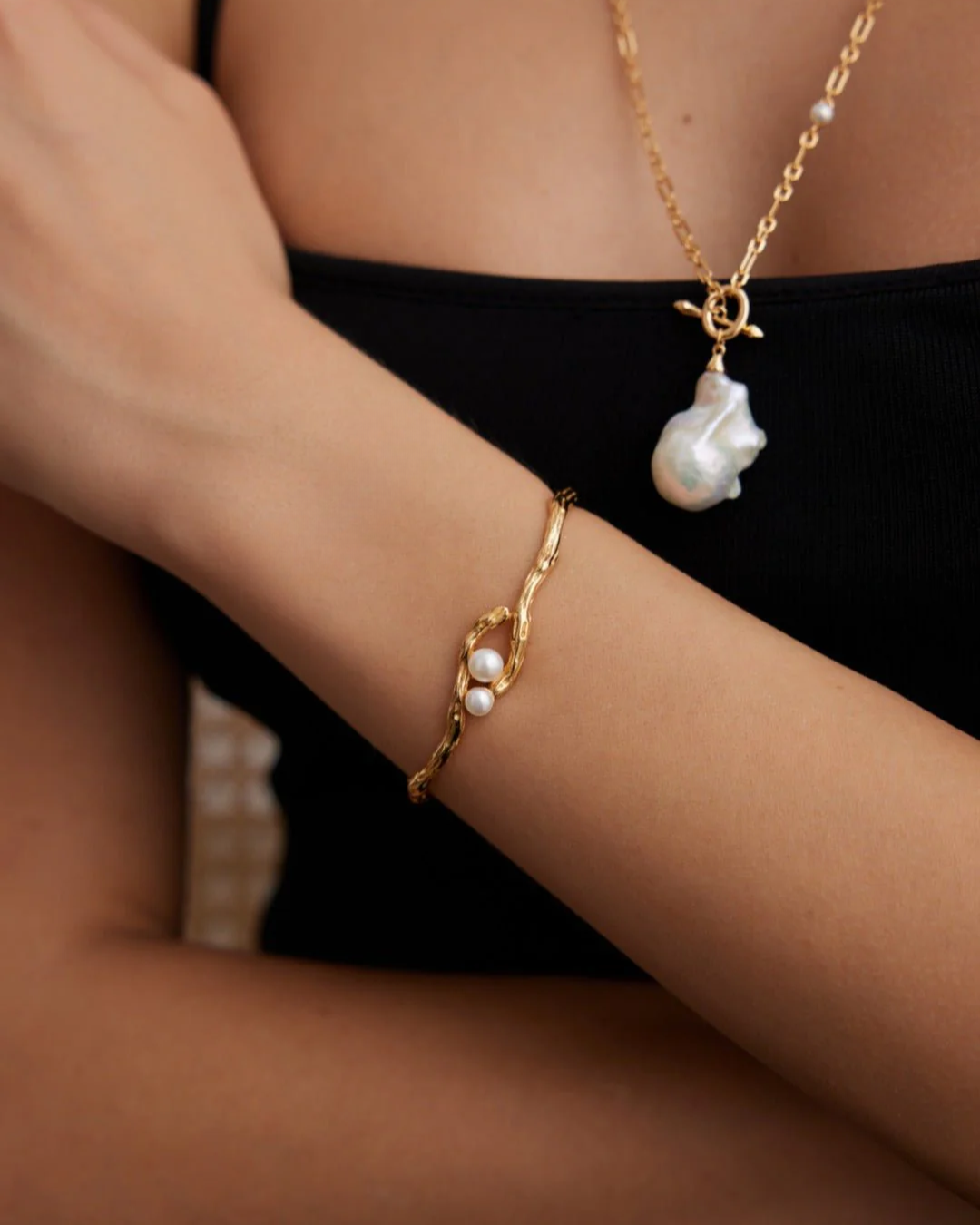 A woman showcasing a beautiful gold bangle paired with a classic pearl necklace, exuding elegance and sophistication.